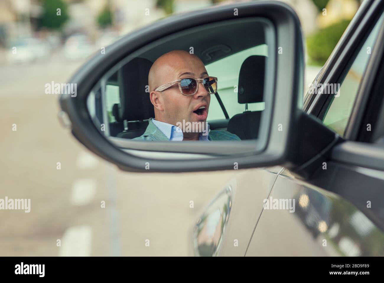 Profilo closeup vista laterale specchio riflettente di bel conducente uomo d'affari che guarda scioccato circa per fare un incidente isolato fondo stradale. Cassaforte t Foto Stock