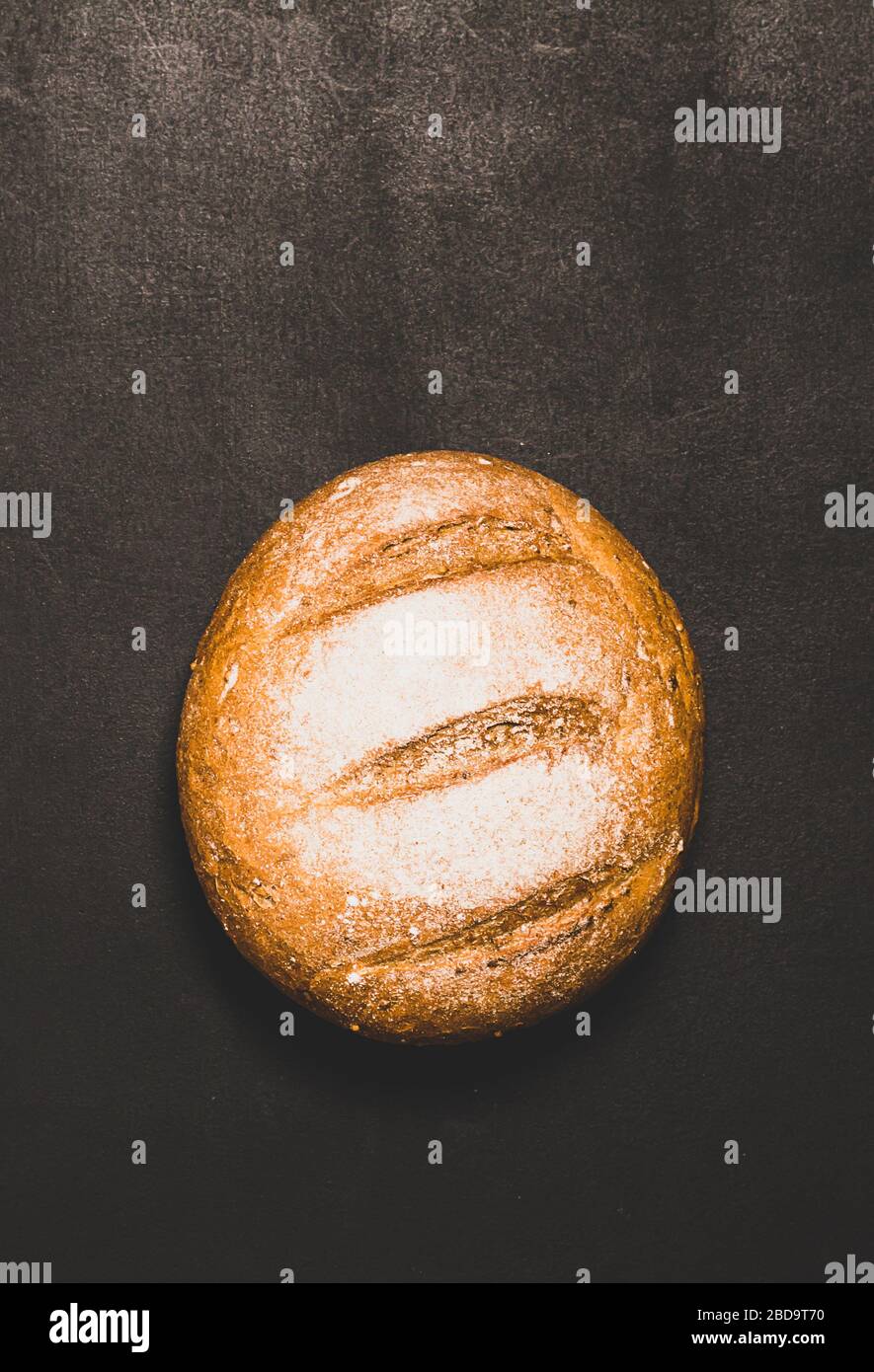 Pane appena sfornato con crosta dorata su sfondo scuro. Concetto di cibo minimalismo. Spazio di copia cornice verticale Foto Stock