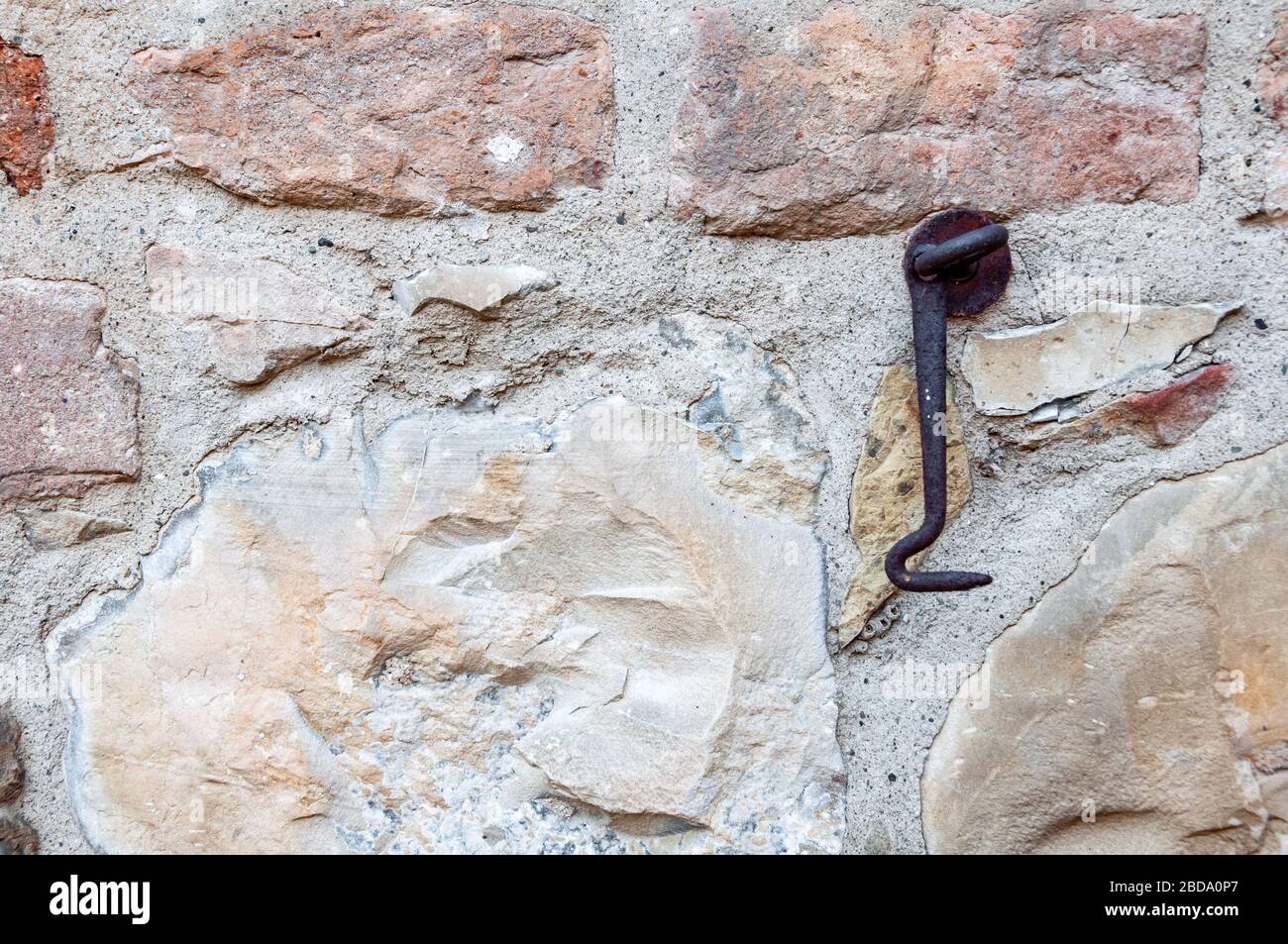 Parete tipica fatta di pietre e mattoni di antica casa italiana, con arrugginito gancio porta di ferro. Foto Stock