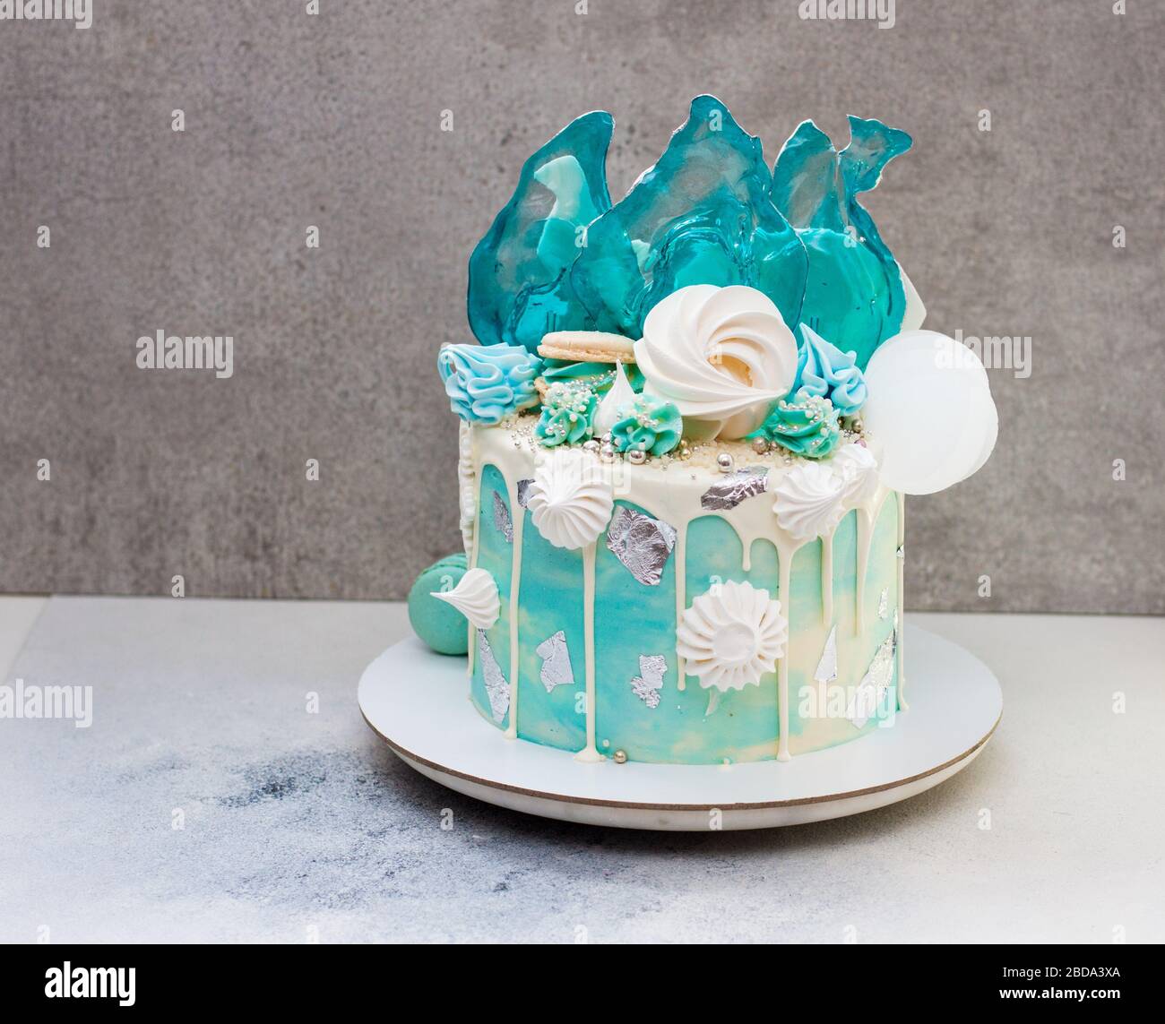 Moderna torta a tema surgelato decorata con caramello blu, cioccolato bianco, fiocchi di neve, macaroon e meringa. Torta di compleanno. Torta invernale isolato Foto Stock