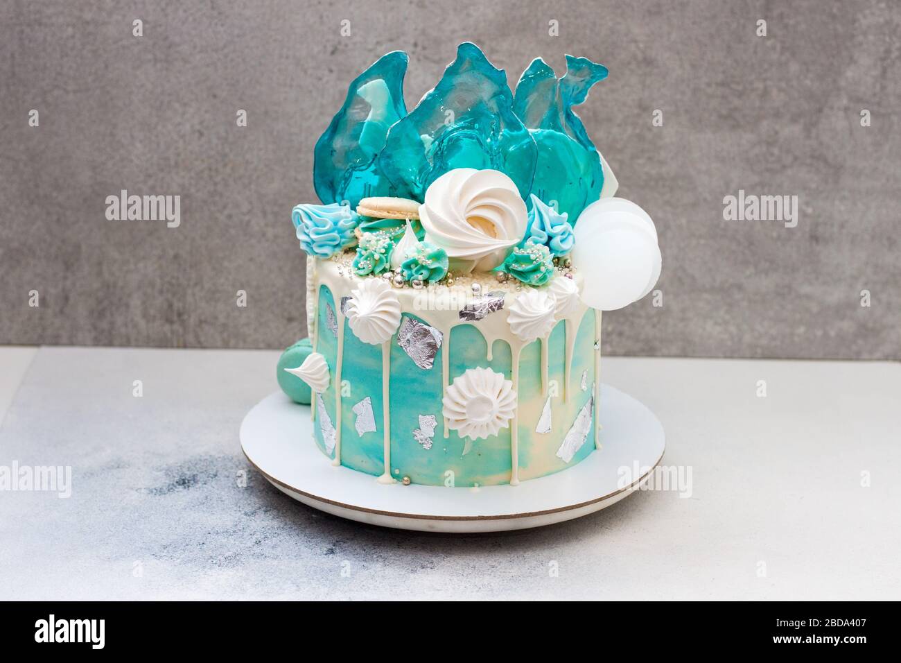 Moderna torta a tema surgelato decorata con caramello blu, cioccolato bianco, fiocchi di neve, macaroon e meringa. Torta di compleanno. Torta invernale isolato Foto Stock