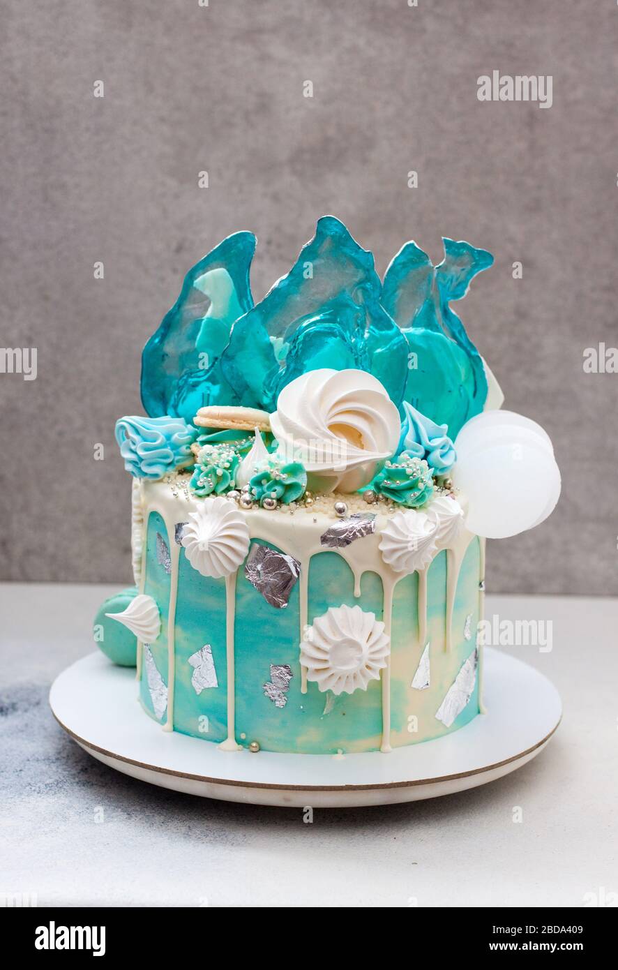 Moderna torta a tema surgelato decorata con caramello blu, cioccolato bianco, fiocchi di neve, macaroon e meringa. Torta di compleanno. Torta invernale isolato Foto Stock
