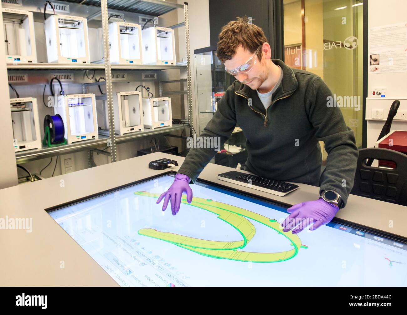 Brian Houston, docente di ingegneria meccanica presso l'Università di Hull, guarda un progetto per un controllo facciale come una banca di stampanti 3D (a sinistra della foto), produrre controlli faccili stampati in 3D per aiutare il personale del servizio sanitario ad affrontare il coronavirus. Foto Stock