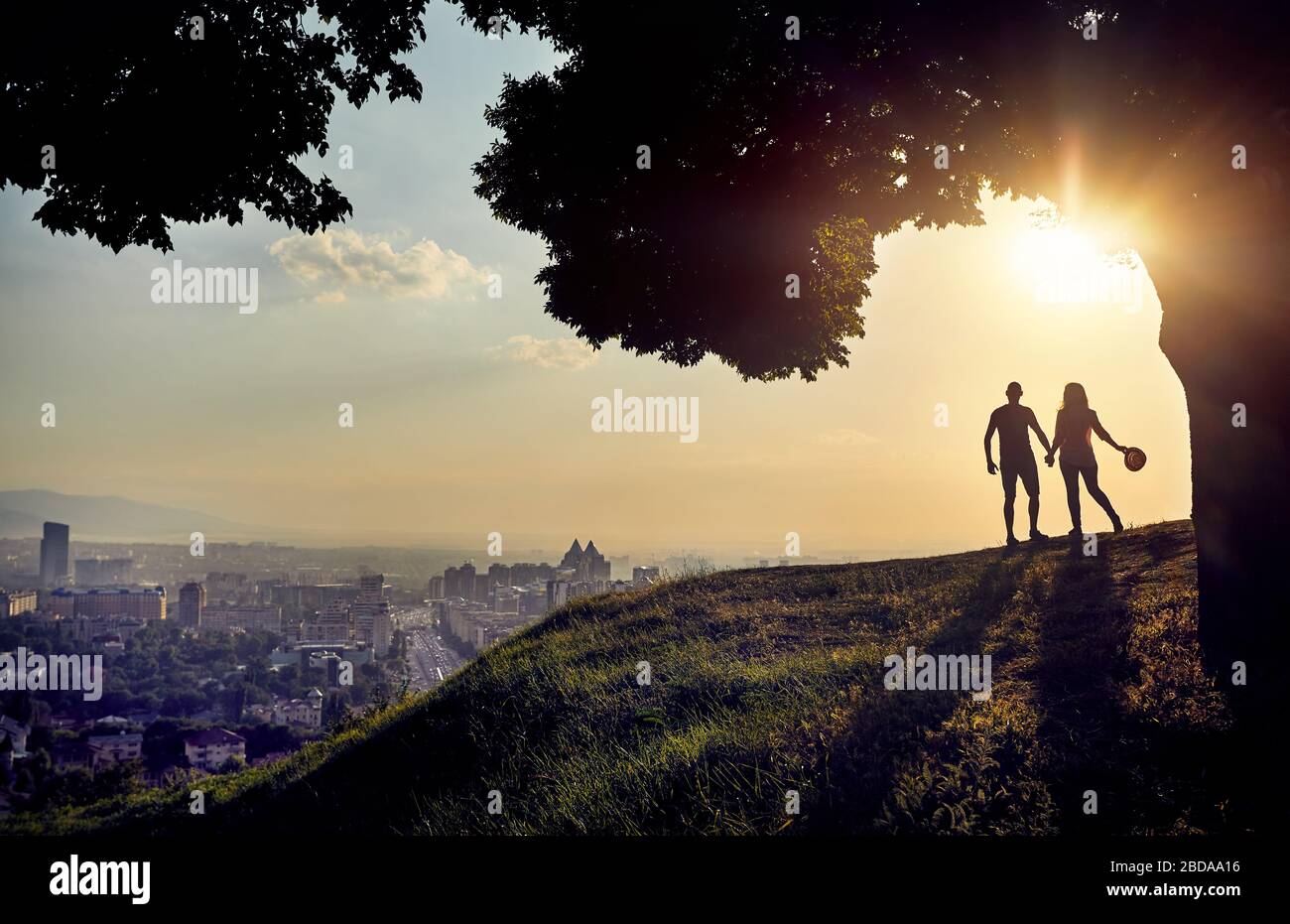 Yong matura in silhouette tenendo premuto dalle mani e guardando il tramonto panorama della città Foto Stock