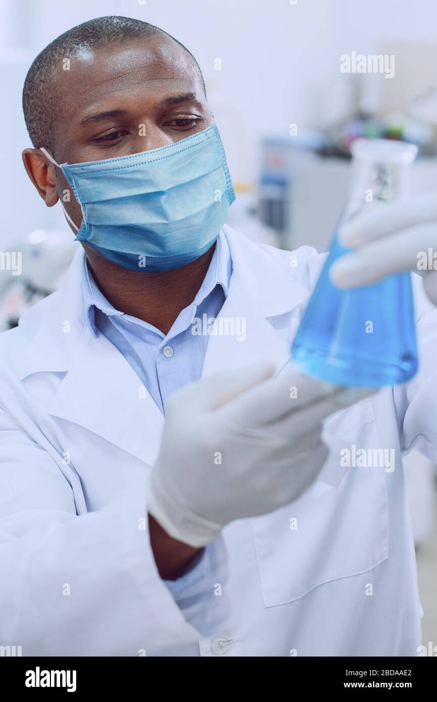 Virologo maschile intelligente che contiene un pallone da laboratorio Foto Stock