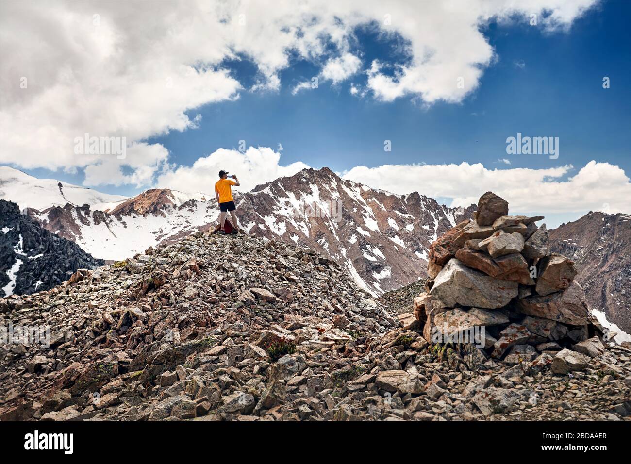 Escursionista in arancione verde t-shirt acqua potabile nelle montagne innevate al cielo blu sullo sfondo Foto Stock