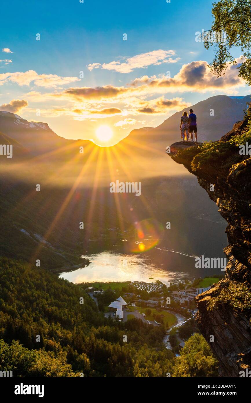 Uomo e donna ammirando il tramonto sul villaggio di Geiranger e Geirangerfjord dalla cima delle rocce, più og Romsdal contea, Norvegia Foto Stock