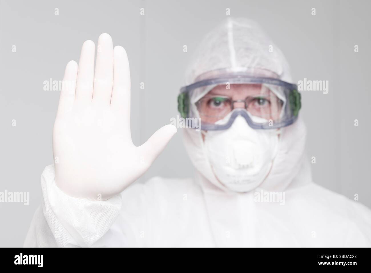 Medico con indumenti protettivi e maschera medica gesturing stop con la sua mano - mettere a fuoco sulla mano Foto Stock