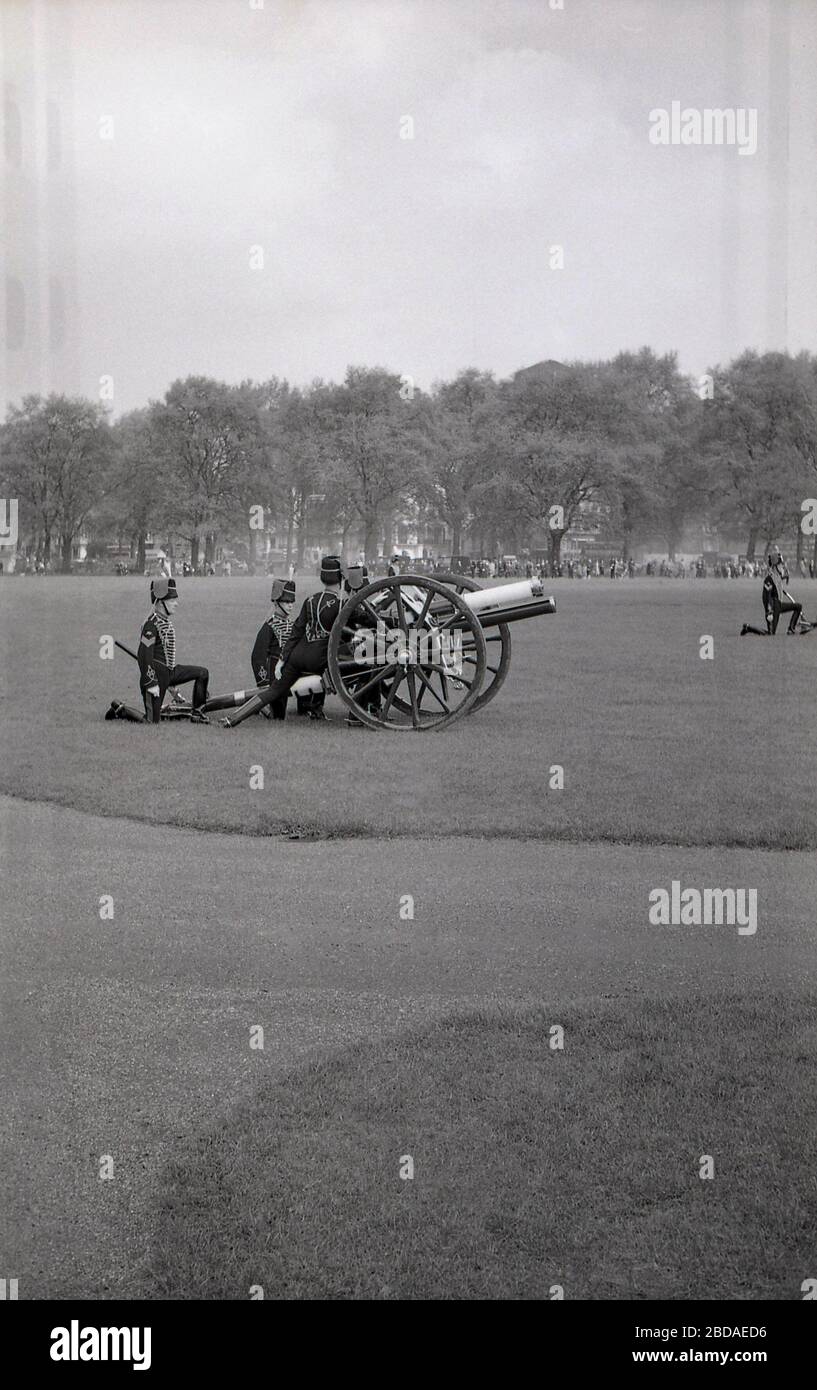 Anni '60, storico, fumo dal fuoco di pistole antiche riempie l'aria in una Royal Gun Salute a Green Park vicino Buckingham Palace, Westminster, Londra, Inghilterra. I saluti delle armi segnano occasioni speciali reali, tra cui il compleanno della Regina, e sono una mostra tradizionale di pageantry britannico. Foto Stock