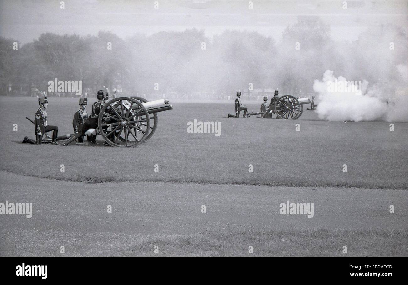 Anni '60, storico, fumo dal fuoco di pistole antiche riempie l'aria in una Royal Gun Salute a Green Park vicino Buckingham Palace, Westminster, Londra, Inghilterra. I saluti delle armi segnano occasioni speciali reali, tra cui il compleanno della Regina, e sono una mostra tradizionale di pageantry britannico. Foto Stock