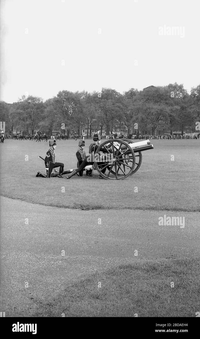 Anni '60, storico, fumo dal fuoco di pistole antiche riempie l'aria in una Royal Gun Salute a Green Park vicino Buckingham Palace, Westminster, Londra, Inghilterra. I saluti delle armi segnano occasioni speciali reali, tra cui il compleanno della Regina, e sono una mostra tradizionale di pageantry britannico. Foto Stock