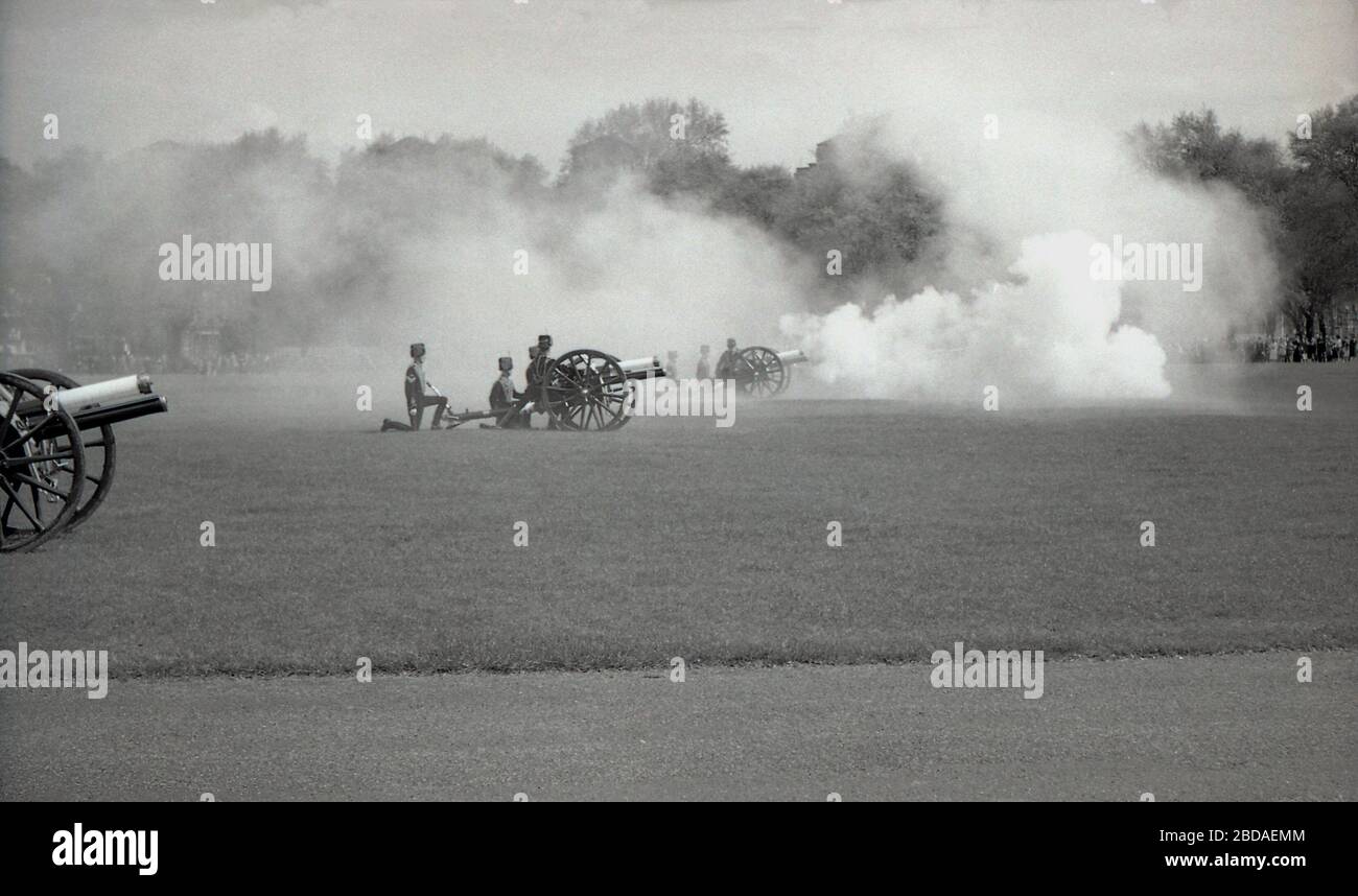Anni '60, storico, fumo dal fuoco di pistole antiche riempie l'aria in una Royal Gun Salute a Green Park vicino Buckingham Palace, Westminster, Londra, Inghilterra. I saluti delle armi segnano occasioni speciali reali, tra cui il compleanno della Regina, e sono una mostra tradizionale di pageantry britannico. Foto Stock