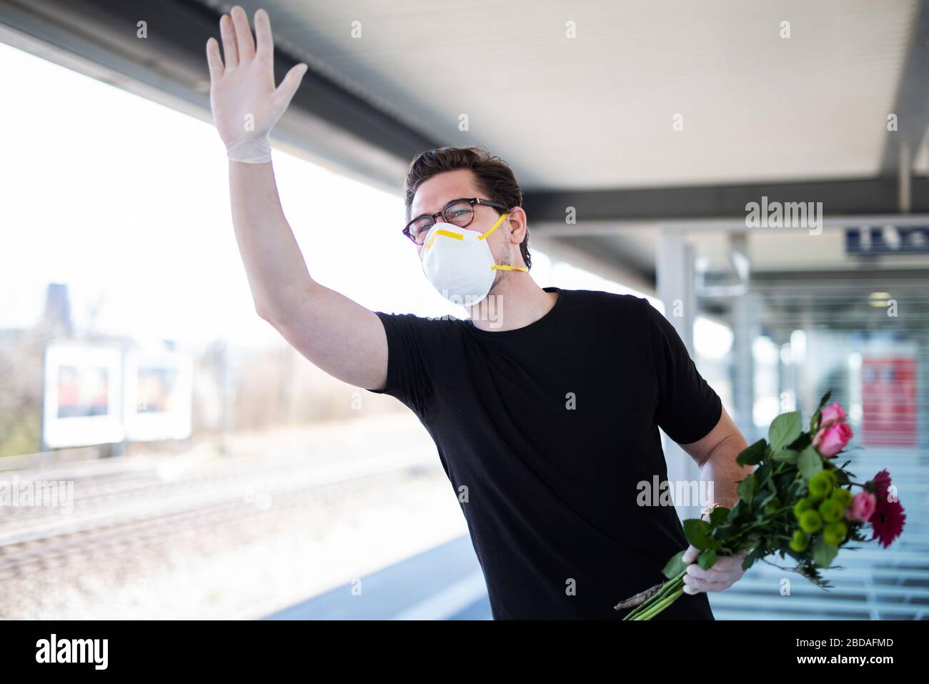 Un uomo raccoglie qualcuno alla stazione ferroviaria in un'era del virus corona con una maschera respiratoria e guanti di gomma Foto Stock
