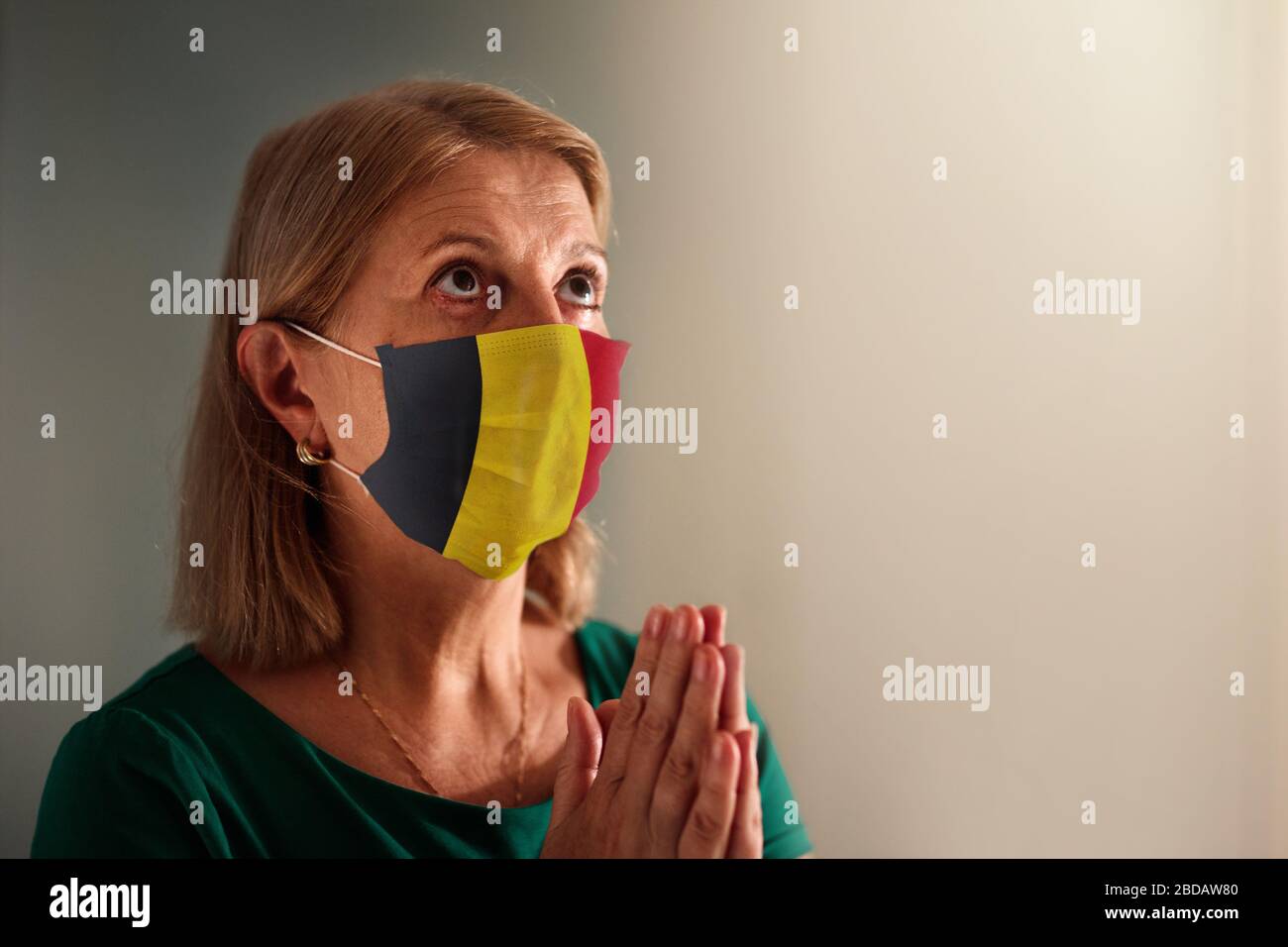 Pregate per il Belgio. Donna in maschera facciale che prega per il popolo belga. Paziente senior nella cappella dell'ospedale o nella chiesa durante l'epidemia di coronavirus. Virus Pandem Foto Stock