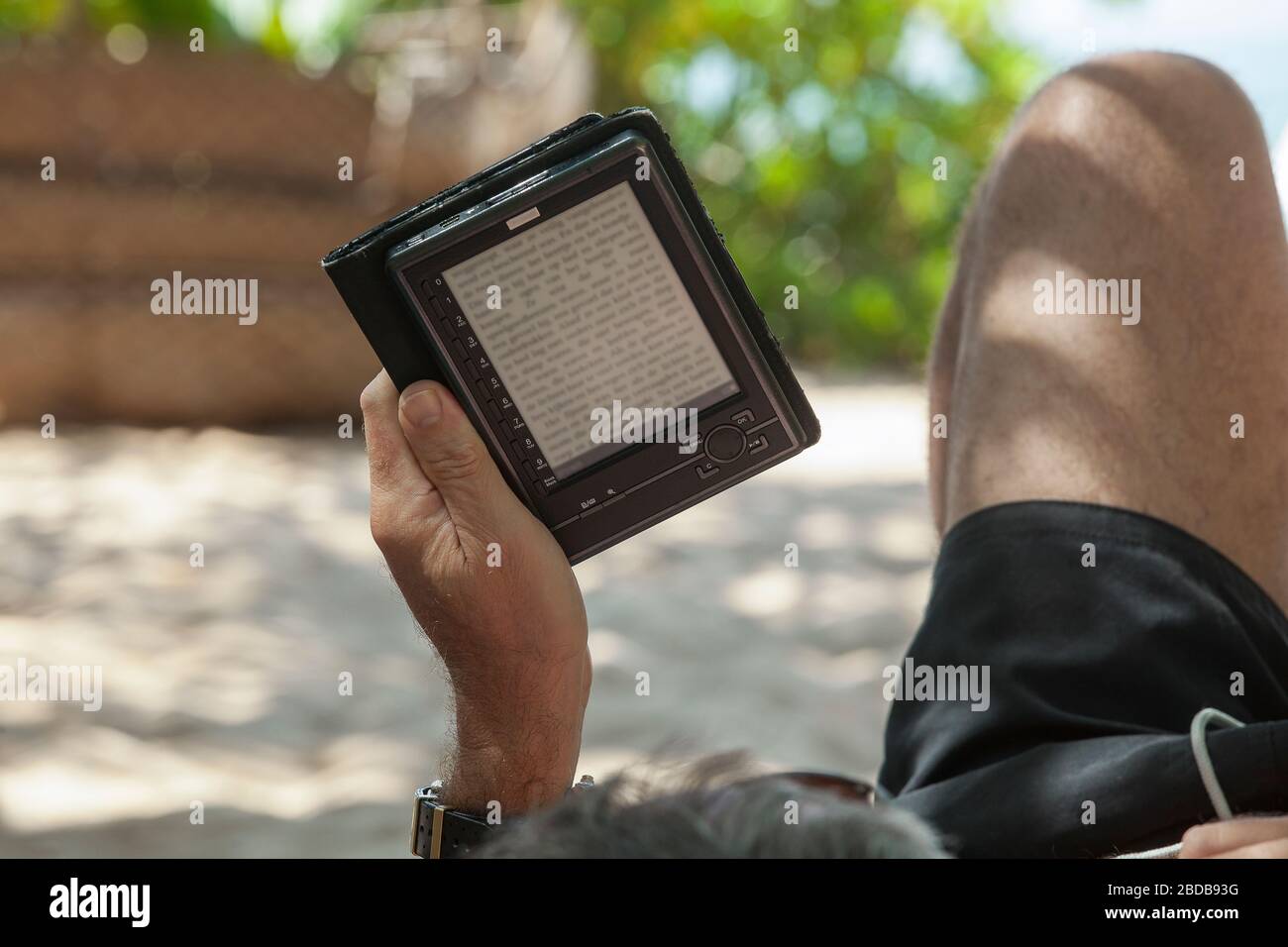 Un uomo che legge su un e-book sulla spiaggia Foto Stock