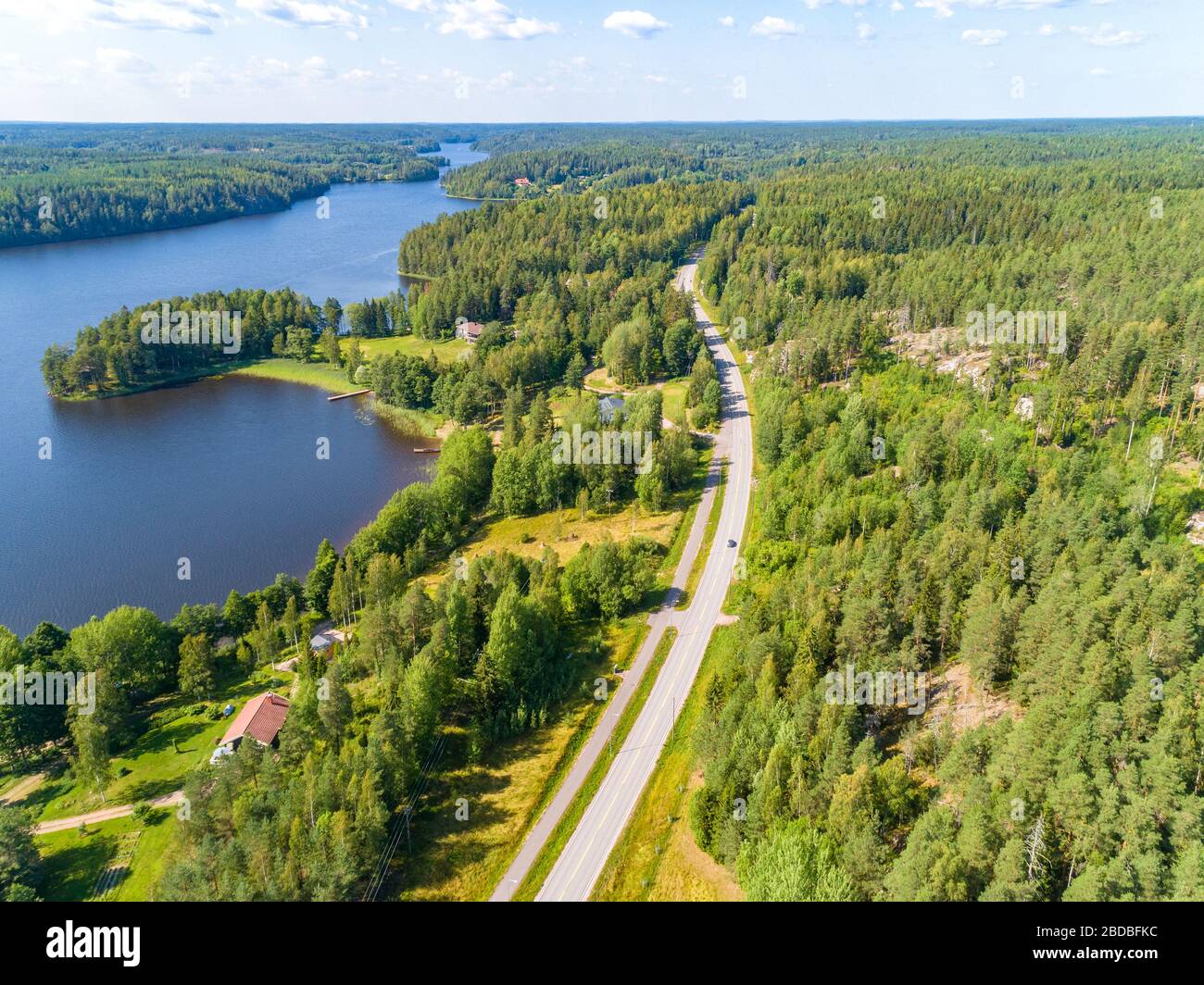 Veduta aerea della strada tra la foresta verde estiva e il lago blu in Finlandia Foto Stock