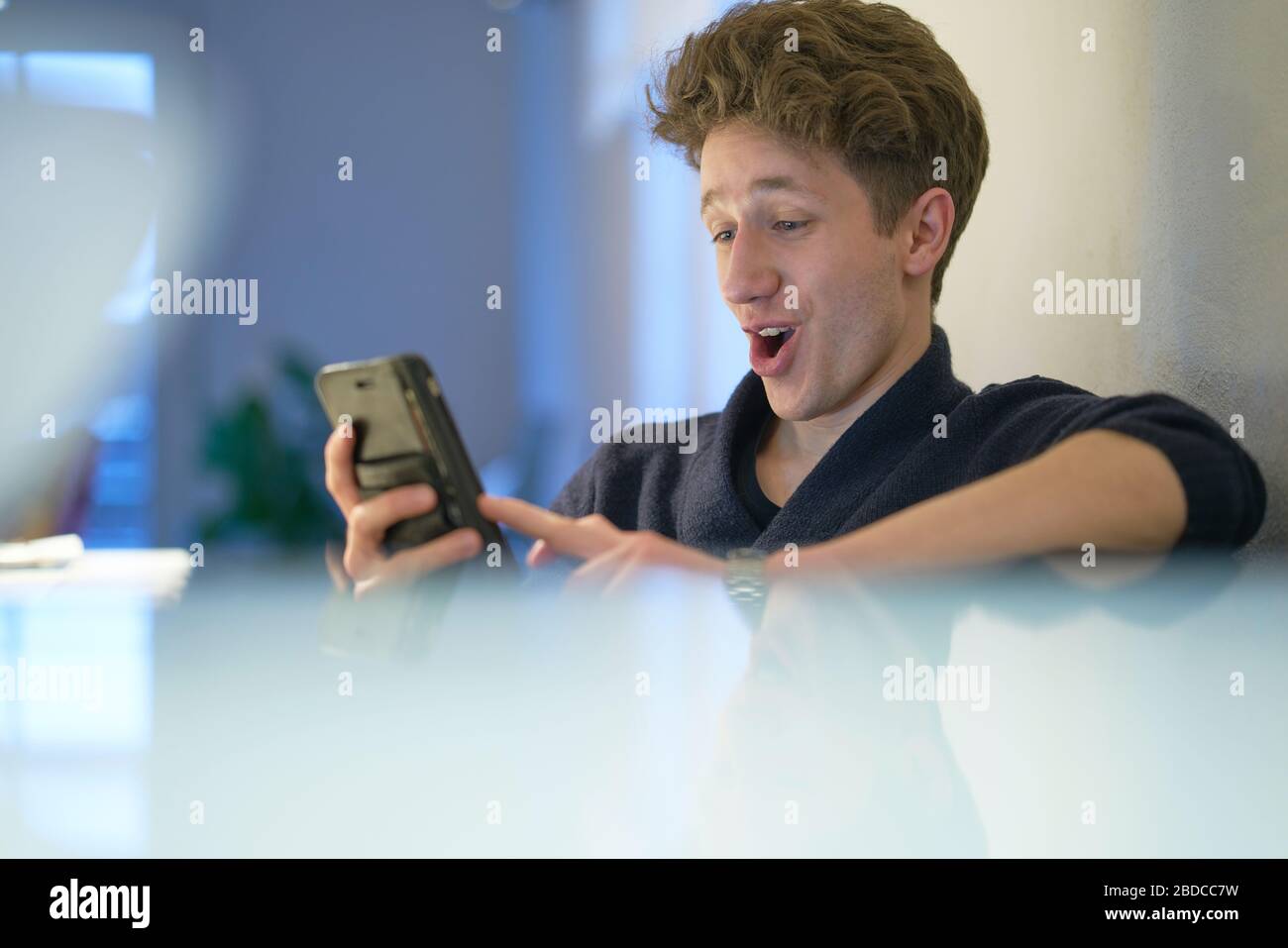 Il giovane uomo è felicemente sorpreso mentre guarda il suo cellulare tra le sue mani Foto Stock