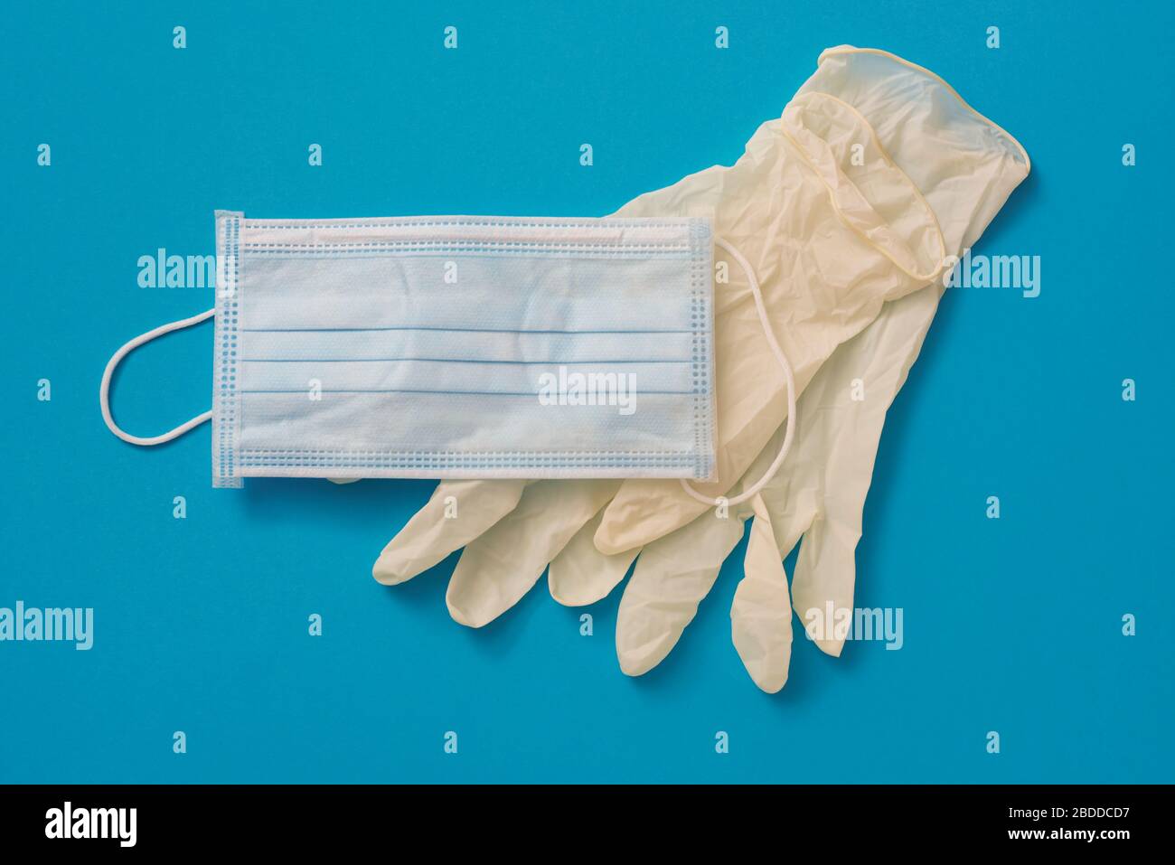 vista ad angolo elevato di un paio di guanti chirurgici monouso e di una maschera chirurgica monouso su sfondo blu Foto Stock