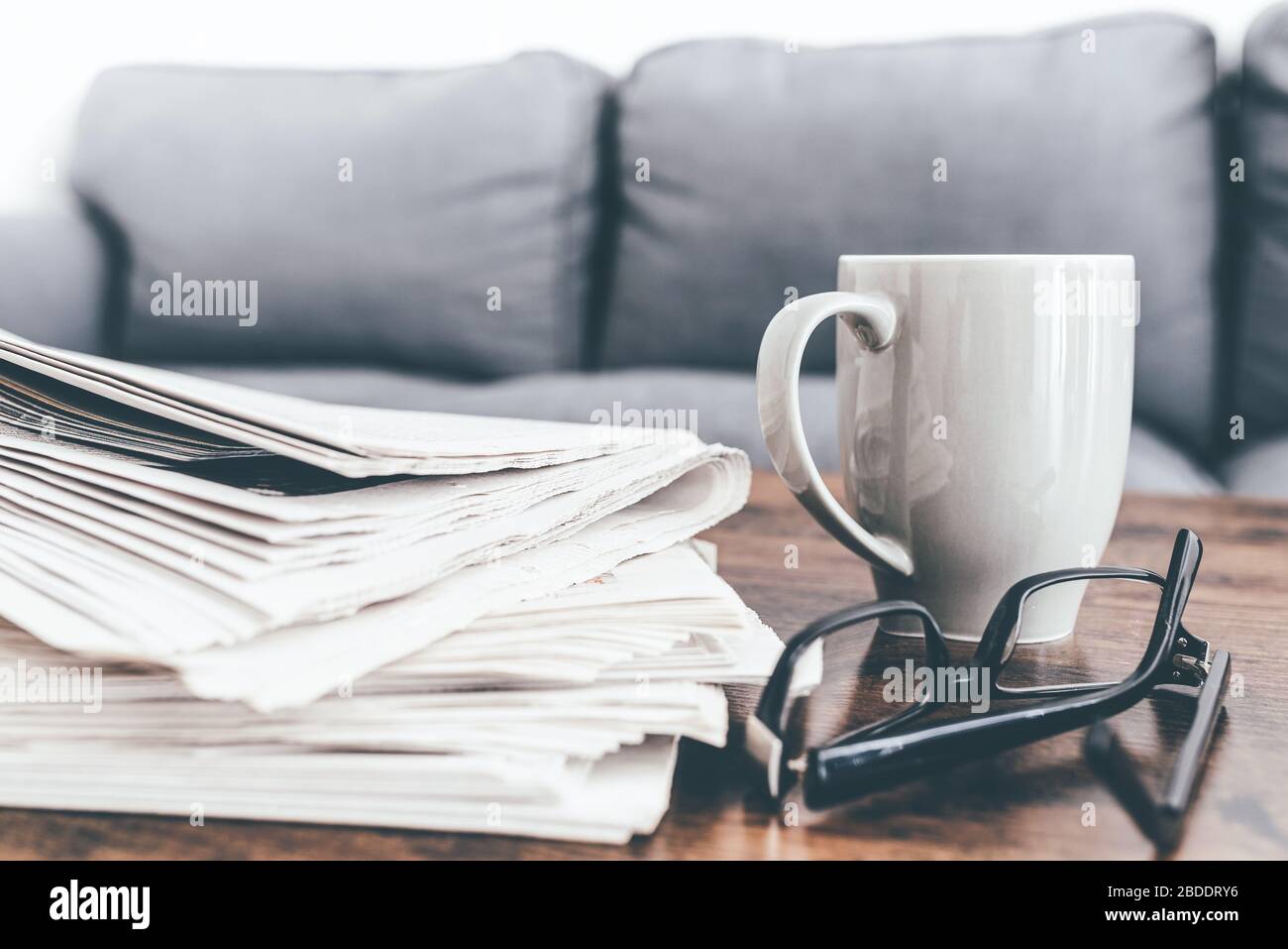 primo piano di una pila di giornali, tazza di caffè e bicchieri sul tavolo del soggiorno. Foto Stock