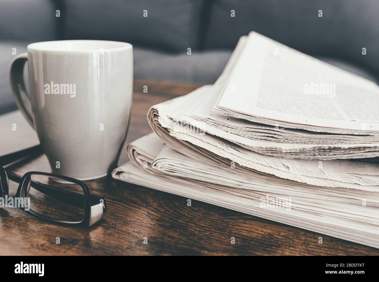 primo piano di una pila di giornali, tazza di caffè e bicchieri sul tavolo del soggiorno Foto Stock