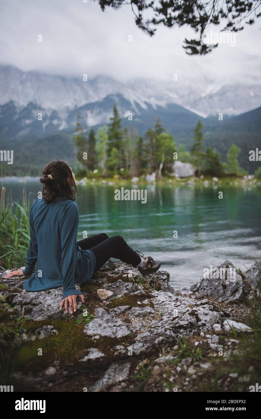 Germania, Baviera, Eibsee, giovane donna seduta sulla roccia sulla riva del lago Eibsee nelle Alpi bavaresi Foto Stock