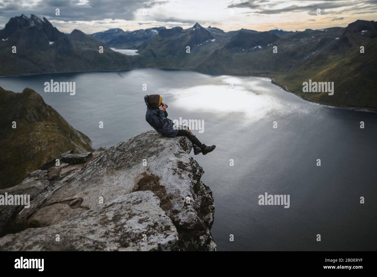Norvegia, Senja, Man scattare foto seduto sul bordo di ripida scogliera sulla cima della montagna Segla Foto Stock