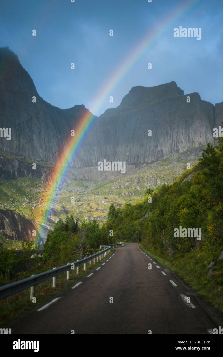 Norvegia, Isole Lofoten, Arcobaleno sopra la strada vuota in paesaggio montano Foto Stock