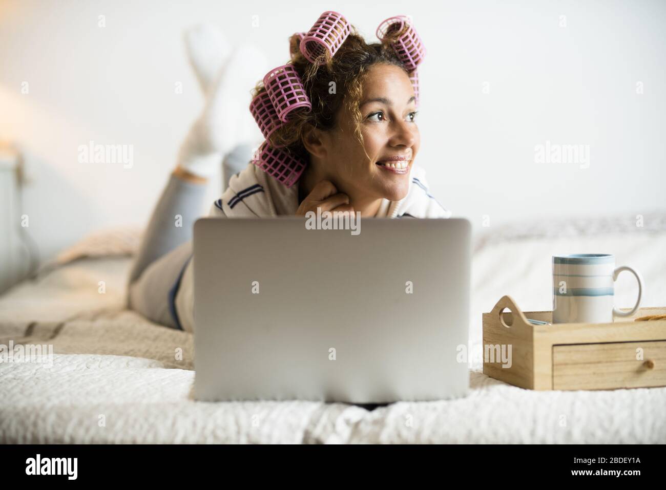 Donna con arricciacapelli sdraiata sul letto con computer portatile Foto Stock