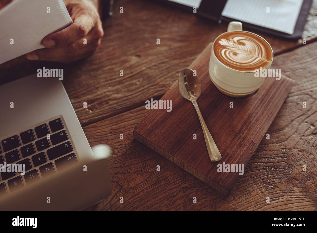 Vista dall'alto di una tazza di caffè caldo cappuccino art su un tavolo di legno con un documento di lettura dell'uomo. Tazza di caffè con disegno artistico in schiuma di latte sul tavolo del caffè Foto Stock