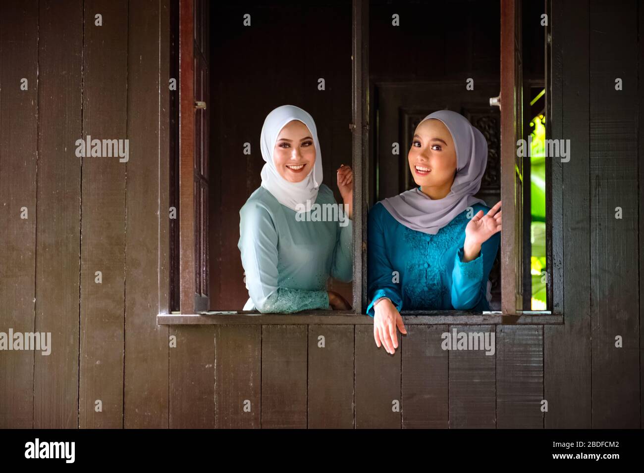 Ritratto di donne malesi musulmane che indossano hijab e costume tradizionale durante le celebrazioni di Aidilfitri alla finestra di legno di una casa tradizionale malese. Foto Stock