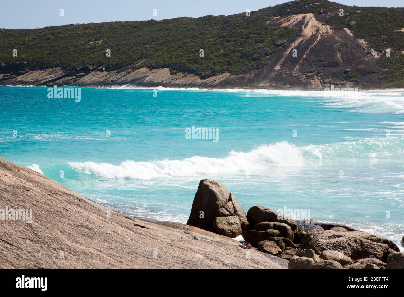 Onde blu, verdi colline e rocce selvatiche e pietre di Hellfire Bay al Cape le Grand National Park nell'Australia occidentale; sneakers indossate in primo piano Foto Stock
