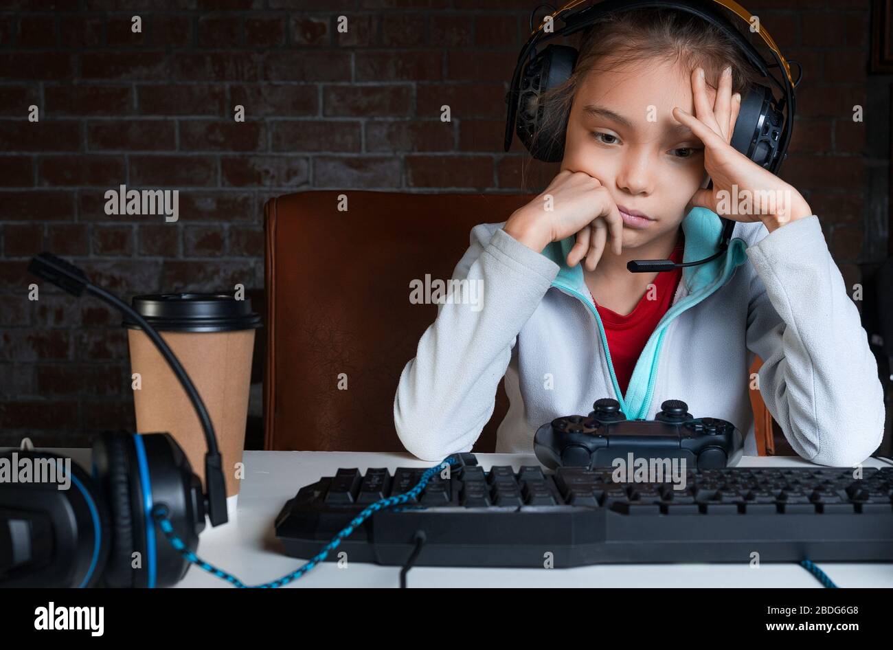 Ragazza seduta di fronte al monitor con video gioco con gamepad con faccia triste. Ha appena perso nel suo gioco preferito. Foto Stock