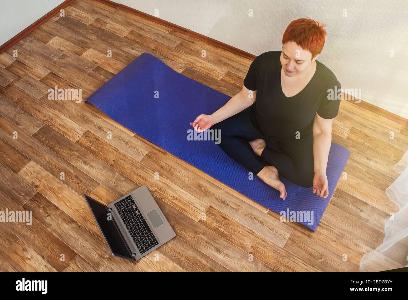 La ragazza adulta pratica online lezione di yoga a casa durante l'isolamento quarantena durante la pandemia coronavirus Foto Stock