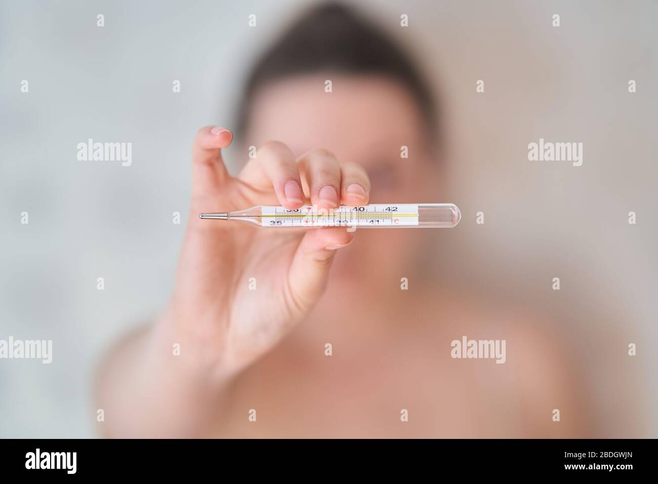 La ragazza tiene un termometro. Temperatura corporea elevata su un termometro. Foto Stock