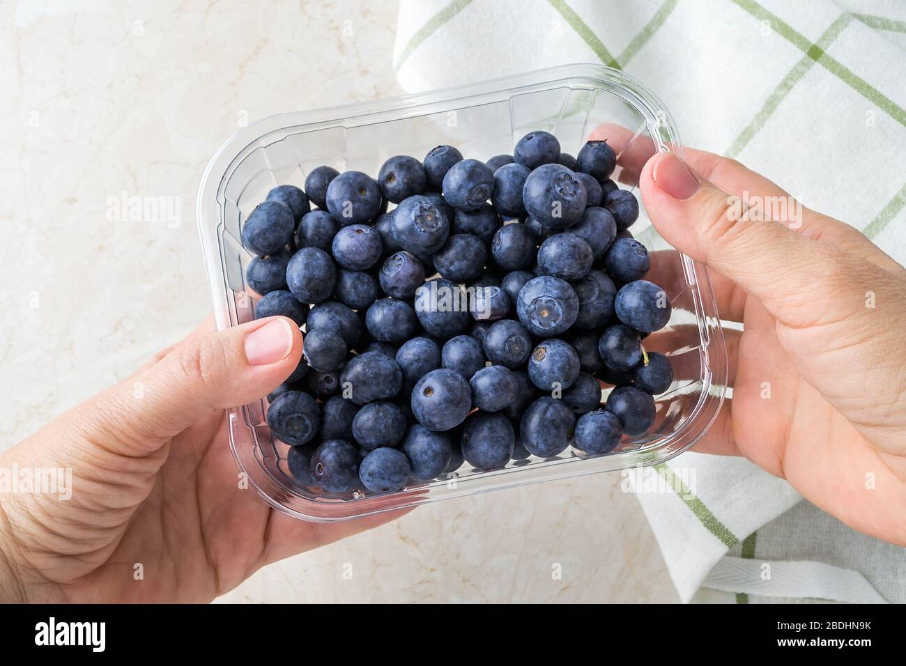 Le mani femminili tengono un contenitore trasparente con mirtilli dolci maturi. Frutta e frutti di bosco, alimentazione vegetariana e sana. Cibo super. Foto Stock