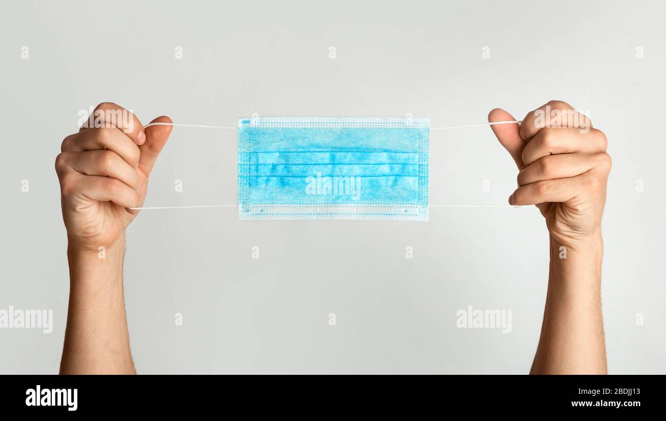 Assistenza sanitaria. Uomo irriconoscibile che tiene maschera medica usa e getta su sfondo bianco, panorama Foto Stock