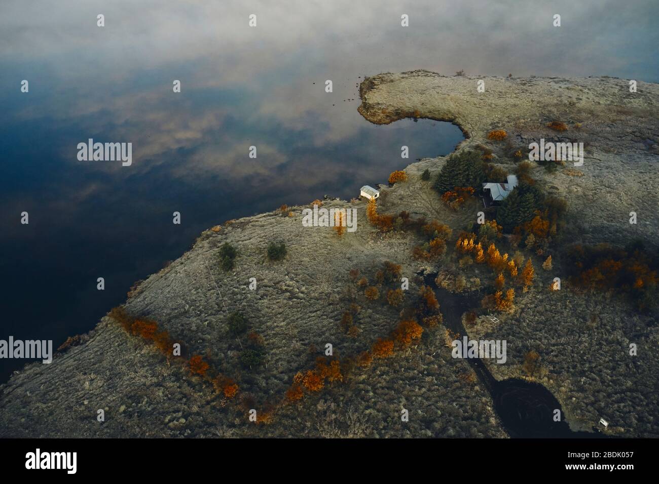 Dall'alto vista aerea di cottage bianchi fattoria situato sulla costa vicino tranquilla lago acqua con riflessione di nuvole in autunno sera in Islanda Foto Stock