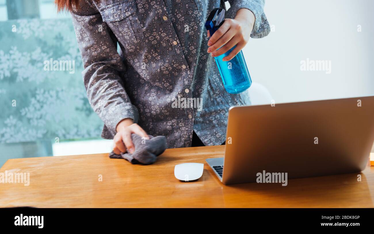 Asian Business giovane donna lavoro da casa ufficio che pulizia computer portatile da sanitizer alcol spray quarantine malattia coronavirus o COVID-19 AN Foto Stock