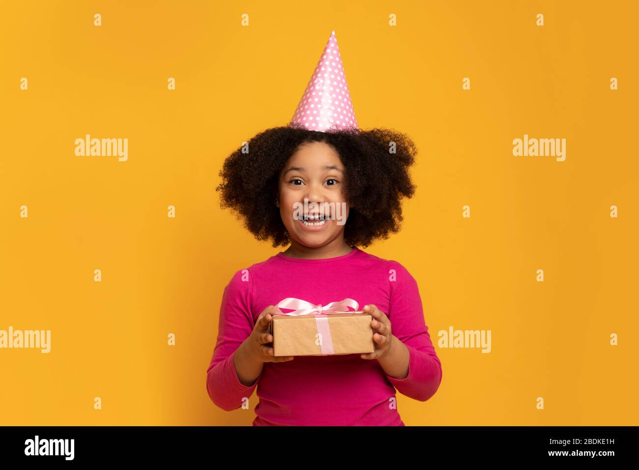 Gioiosa bambina Afro Birthday Girl che indossa Party Hat e Holding presente Foto Stock