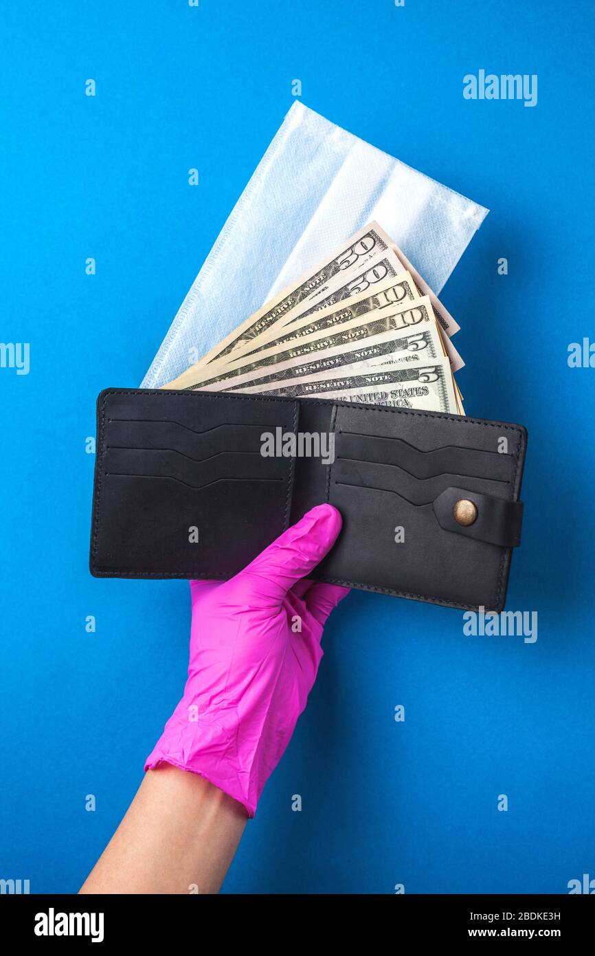 Mano in gomma guanti tiene una tosse con maschera medica e denaro. Scudo facciale medico e denaro americano. Il concetto di crisi finanziaria globale. Assistenza finanziaria per la medicina Foto Stock