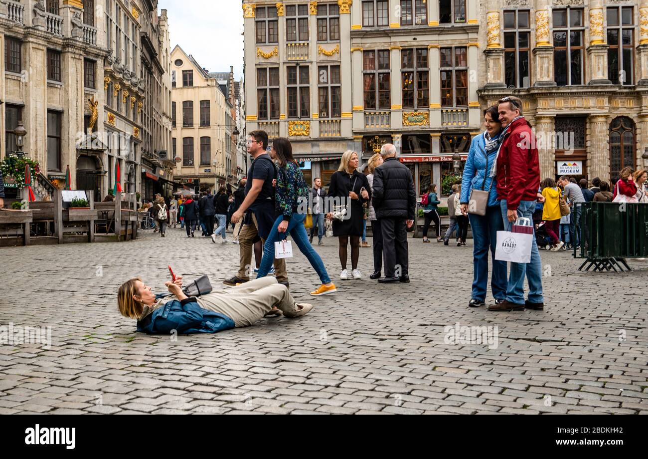 Bruxelles, Belgio - Ottobre 12 2019: Donna turistica scattando foto dei suoi amici via cellulare sdraiato a terra in grande luogo Foto Stock