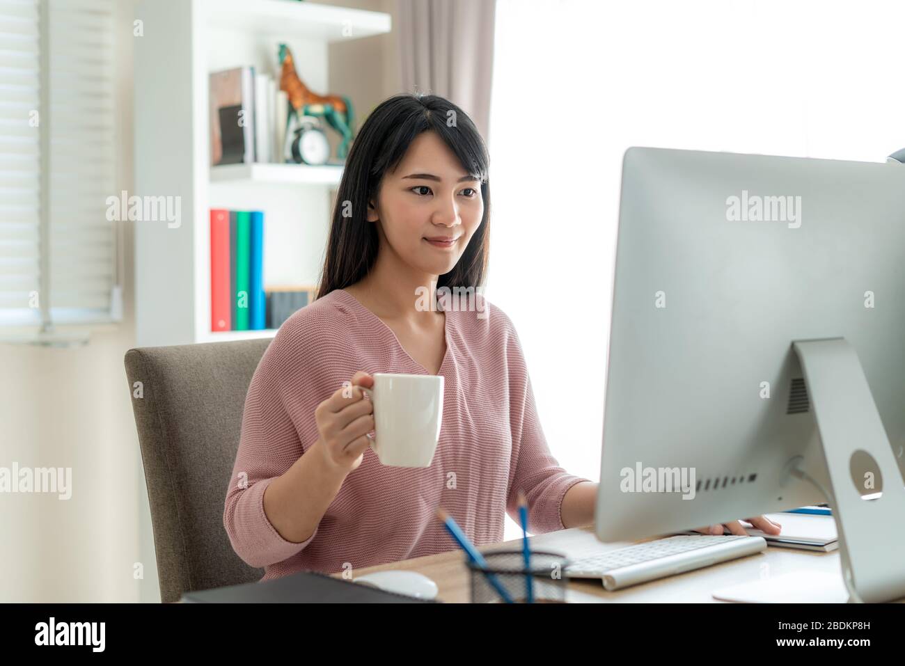 Asian bella giovane donna lavorare da casa lavorare sul computer e bere caffè mentre si lavora in soggiorno a casa. Stile di vita di distanza sociale i Foto Stock