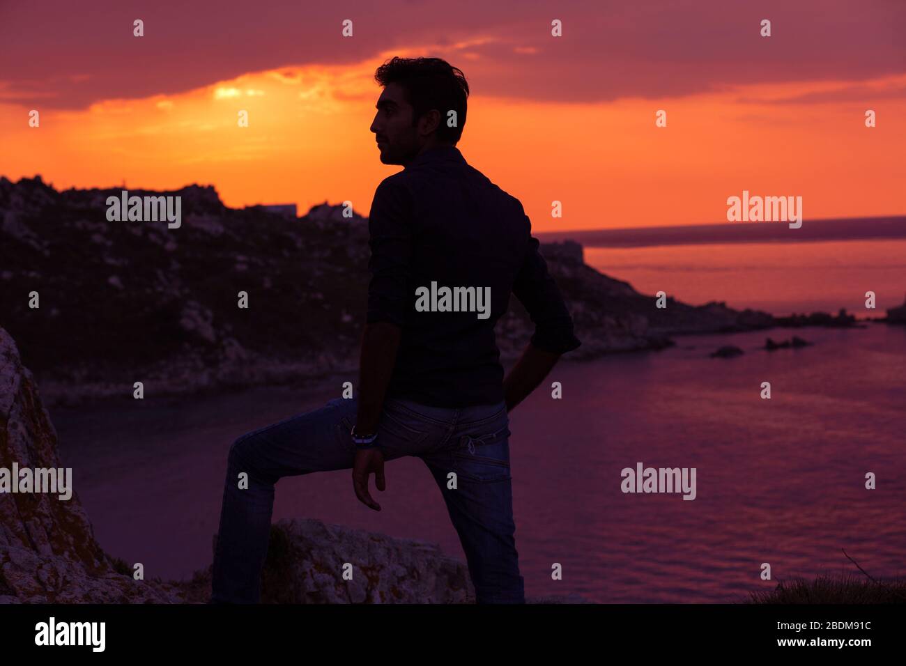 uomo in piedi pensare indietro luce tramonto illuminazione vista laterale profilo silhouette estate sera spiaggia Foto Stock