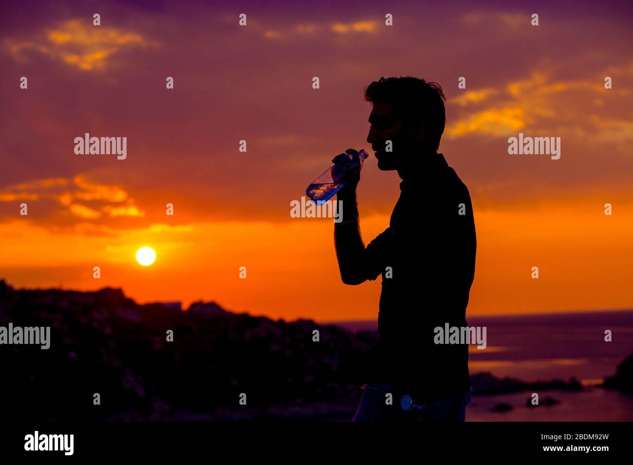 Profilo dell'uomo silhouette bere acqua da una bottiglia al tramonto con il sole sullo sfondo Foto Stock