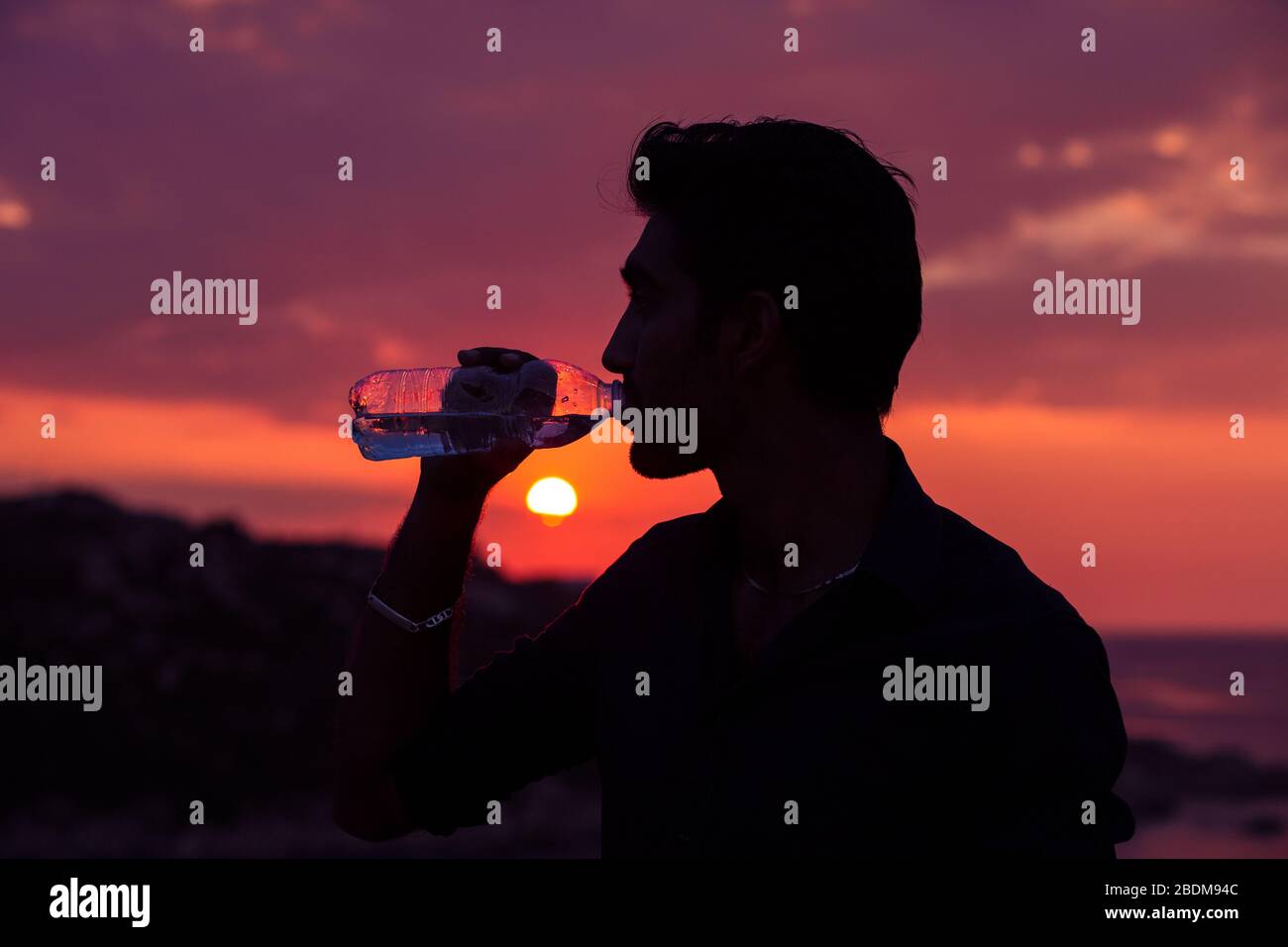 Profilo dell'uomo silhouette bere acqua da una bottiglia al tramonto con il sole sullo sfondo Foto Stock