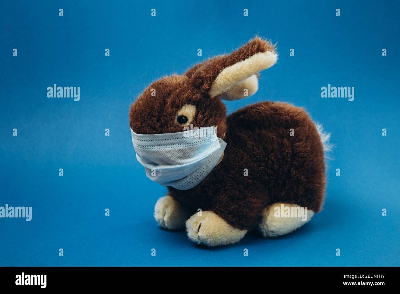 Il coniglio giocattolo si trova in una maschera medica su sfondo blu. Concetto di protezione da malattie respiratorie, virus e protezione individuale delle vie respiratorie. Interrompere il coronavirus. Foto Stock