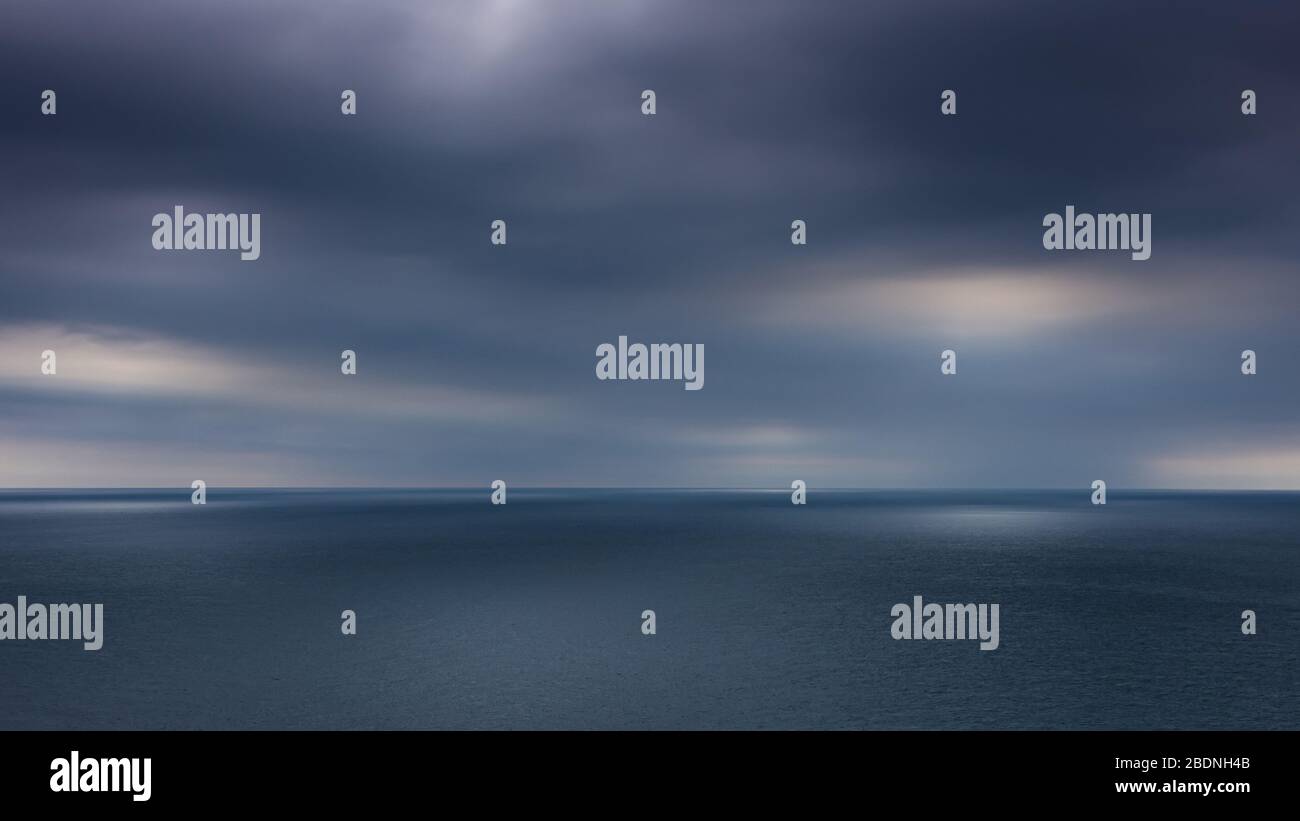 Guardando fuori all'orizzonte dell'oceano dalla testa di St Alban mentre il sole cerca di rompere attraverso le nuvole scure e umide, Dorset, Regno Unito Foto Stock