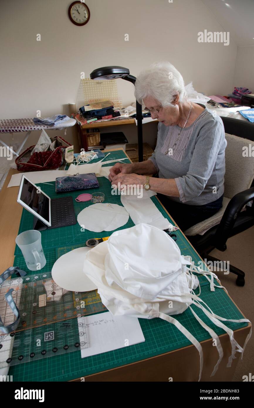 Donna anziana che fa i cappelli dei dispositivi di protezione personale (PPE) per il NHS nella crisi di Covid-19 Foto Stock