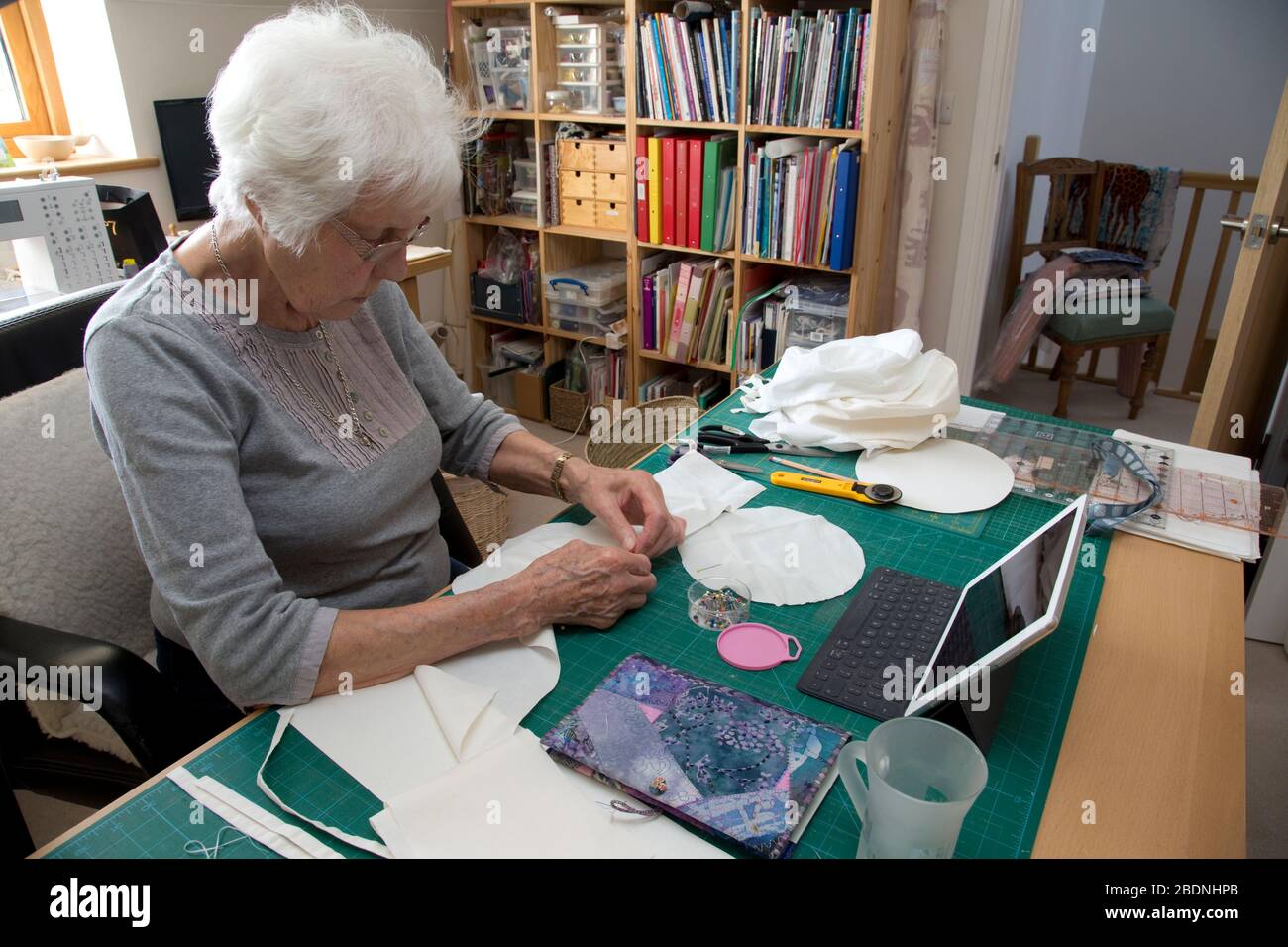 Donna anziana che fa i cappelli dei dispositivi di protezione personale (PPE) per il NHS nella crisi di Covid-19 Foto Stock