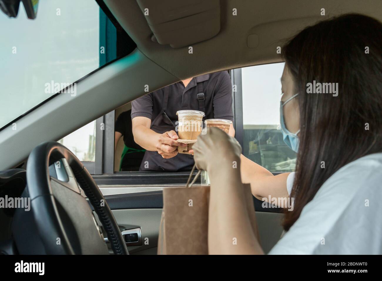 Donna in maschera protettiva prendere il caffè a drive thru durante lo scoppio del covid-19. Foto Stock